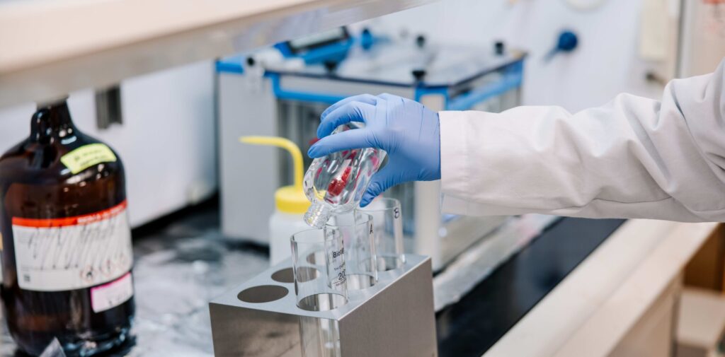 Hand pouring liquid from a bottle into another container.
