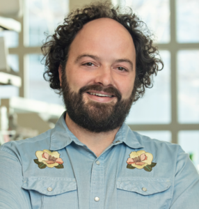 Man with brown hair and beard wearing a blue button up shirt