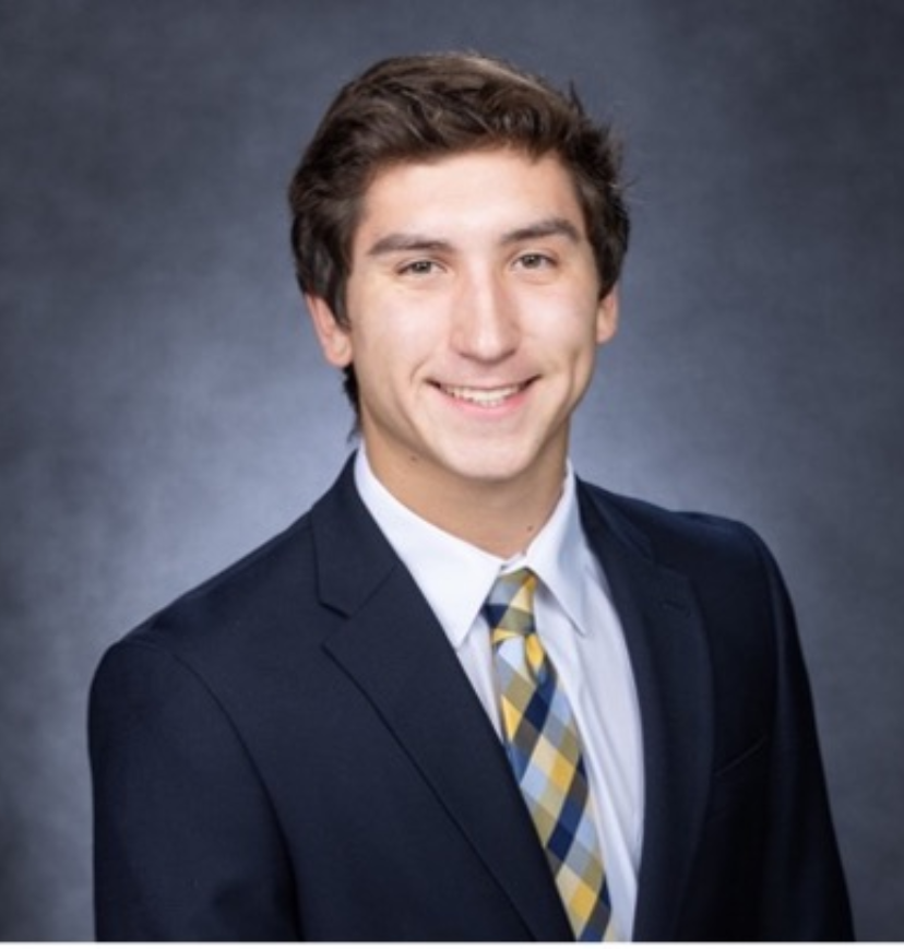 Young man with brown hair wearing a suit and smiling.