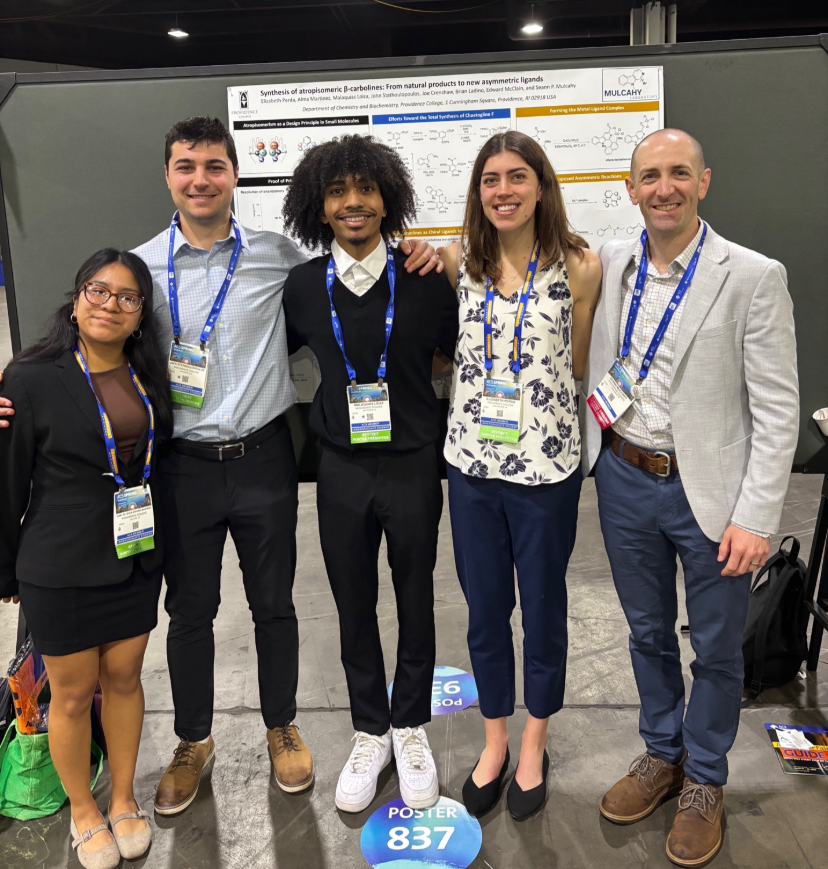 Five smiling people standing together in front of an scientific poster.