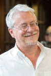 Man with white hair and glasses smiling.