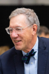A man with grey hair and glasses wearing a suit and bow tie.
